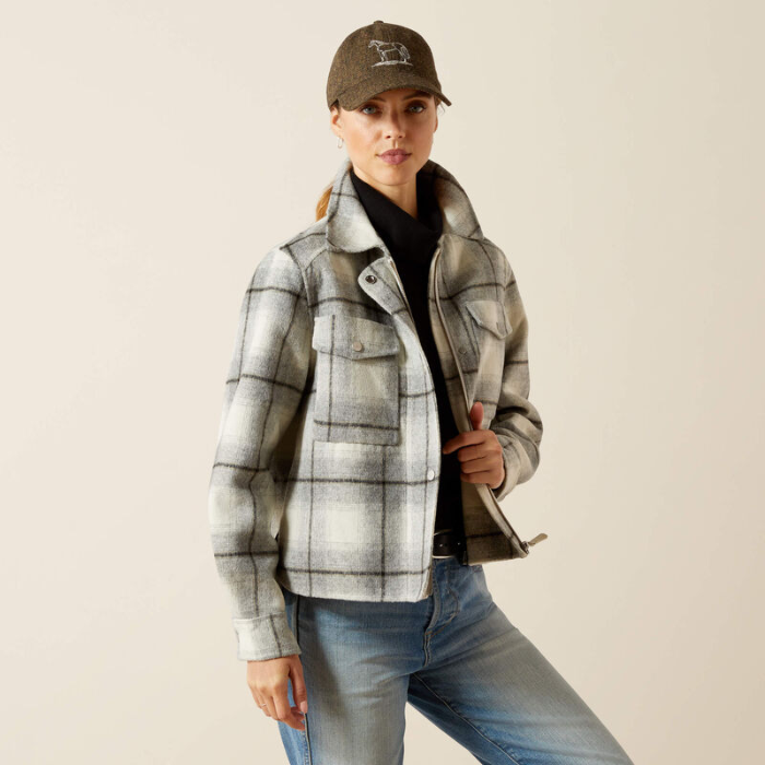 Person wearing a plaid jacket, jeans, and a cap on a beige background