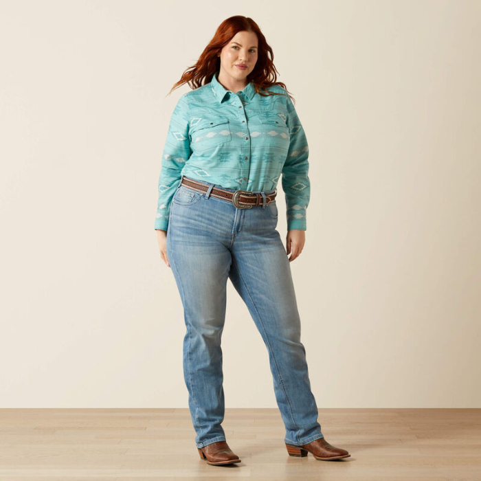 Woman wearing a light blue patterned shirt and jeans on a plain background