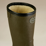 Green wellington boot with black trim and Chameau logo on a beige background