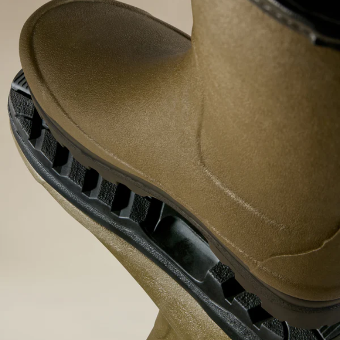Close-up of a brown-green boot with a black sole on a beige background