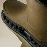 Close-up of a brown-green boot with a black sole on a beige background