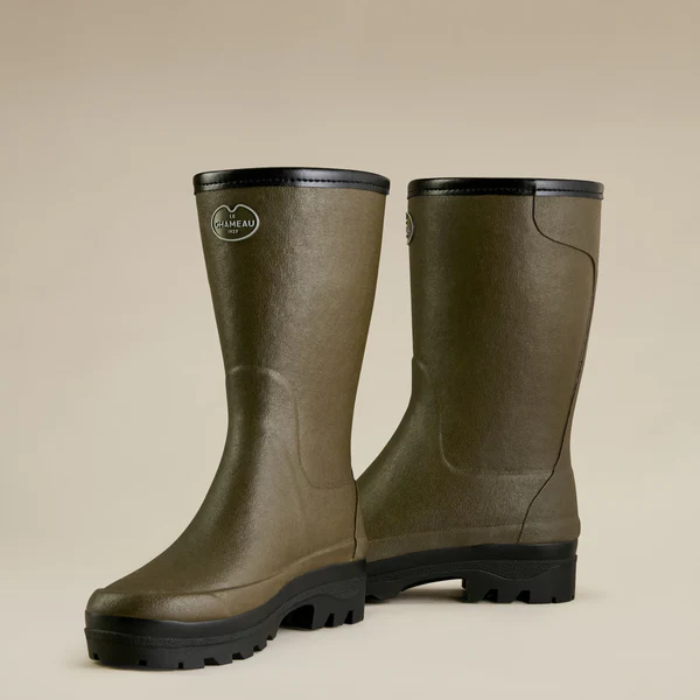 Pair of green rubber boots with black soles on a beige background