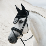 White horse wearing a black ear bonnet on a sandy background