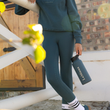 Person wearing teal outfit holding a black water bottle with 'LeMieux' branding, standing on a staircase.