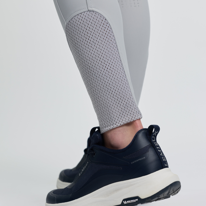 Navy athletic shoe with white sole worn by a person in grey leggings on a light grey background