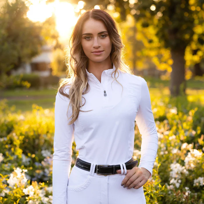 Woman in a white outfit standing in a garden with sunlight filtering through the trees.
