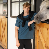 Man wears a green t-shirt and black casual trousers standing near a stable and white pony