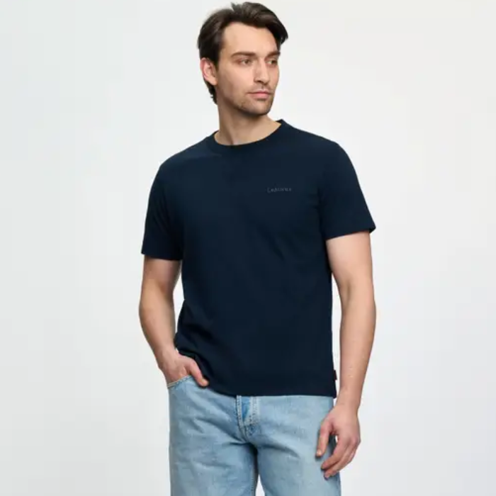 Man wears a navy t-shirt and light jeans on a white background
