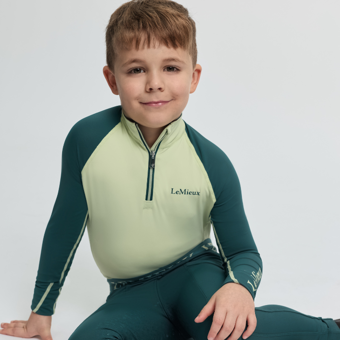 Child wearing a green and yellow equestrian outfit with 'LeMieux' branding on a white background