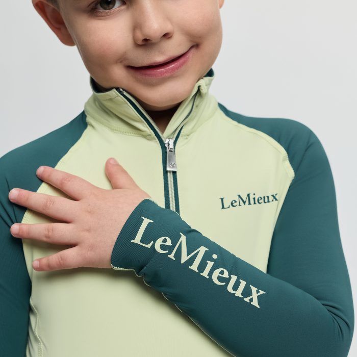 Child wearing a green and yellow LeMieux outfit with one arm crossed over the chest.