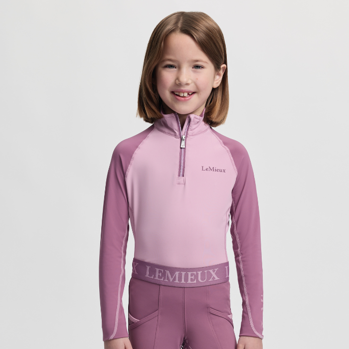 Young girl wearing a pink and purple LeMieux equestrian outfit on a light grey background