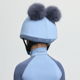Person wearing a light blue equestrian helmet with fur pom-poms on a plain background