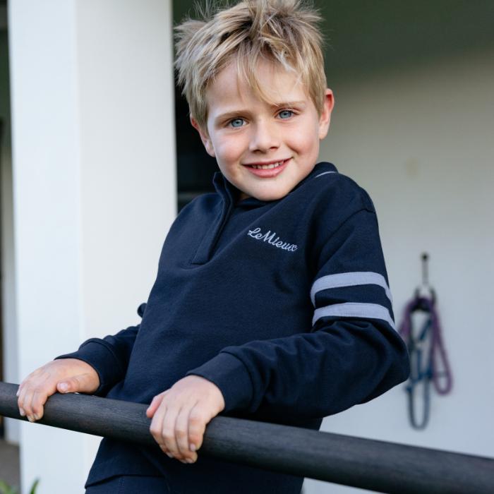 Young boy wearing a navy blue sweatshirt with a brand logo, standing outdoors.