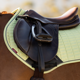Brown saddle with a yellow saddle pad against a blurred outdoor setting