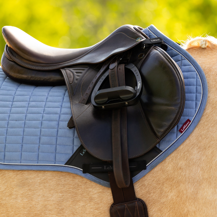 Brown saddle on a blue saddle pad with a blurred green background