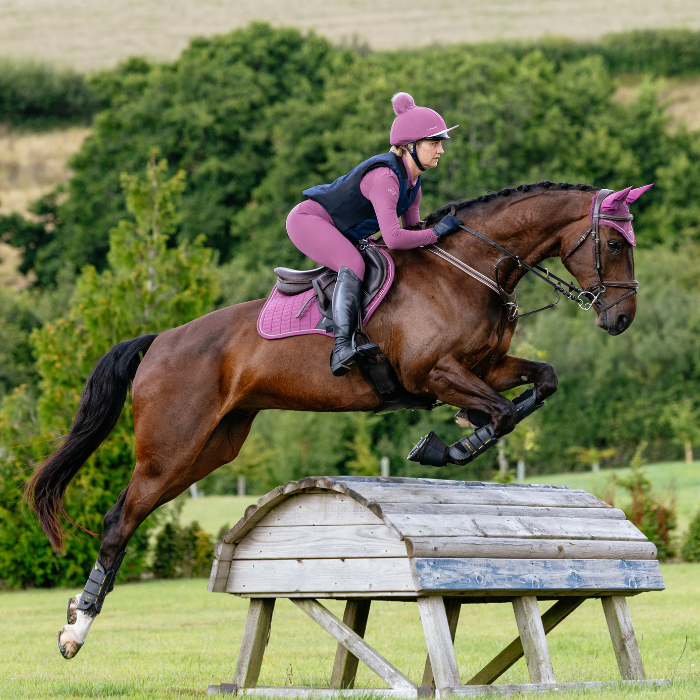 Horse and rider jumping over a wooden obstacle in an outdoor setting