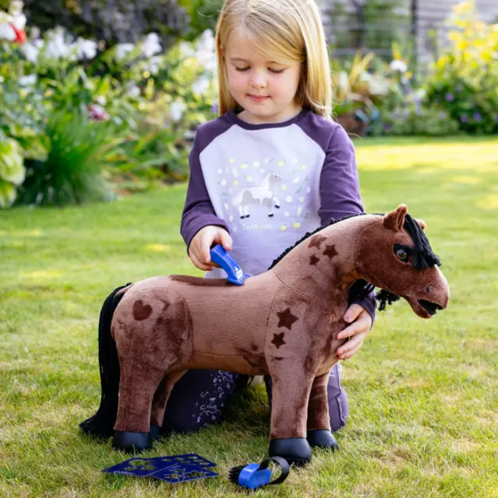 Little girl plays with a blush toy pony and accessories in a garden setting