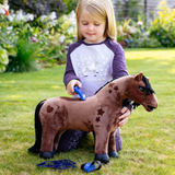 Little girl plays with a blush toy pony and accessories in a garden setting