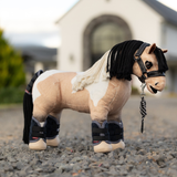 Plush toy horse with bridle and boots on a gravel surface