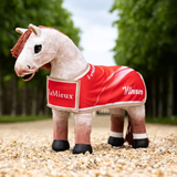 Toy pony wears a red rug with LeMieux and Winner detailing against an outdoor setting 