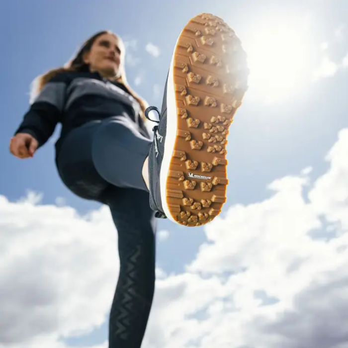 Person wearing a navy trainer with a focus on the sole against a blue sky.