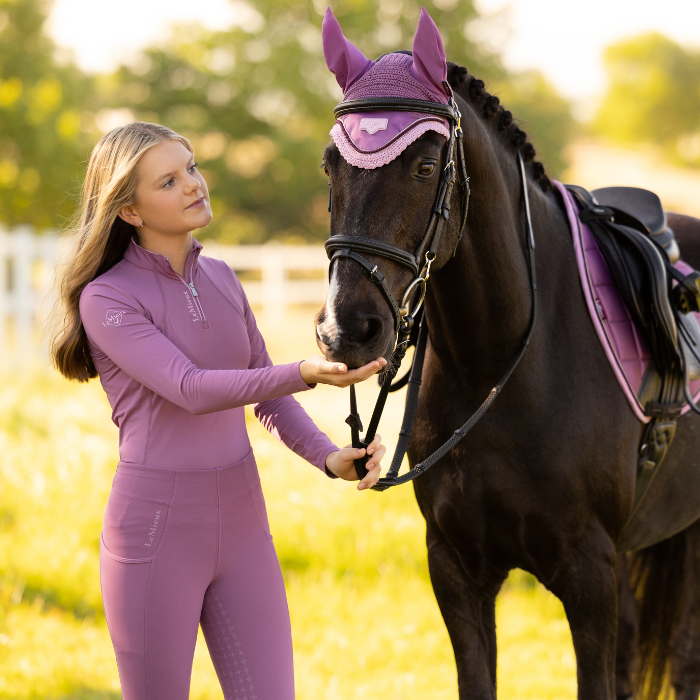 Woman in pink equestrian gear standing next to a horse in a field