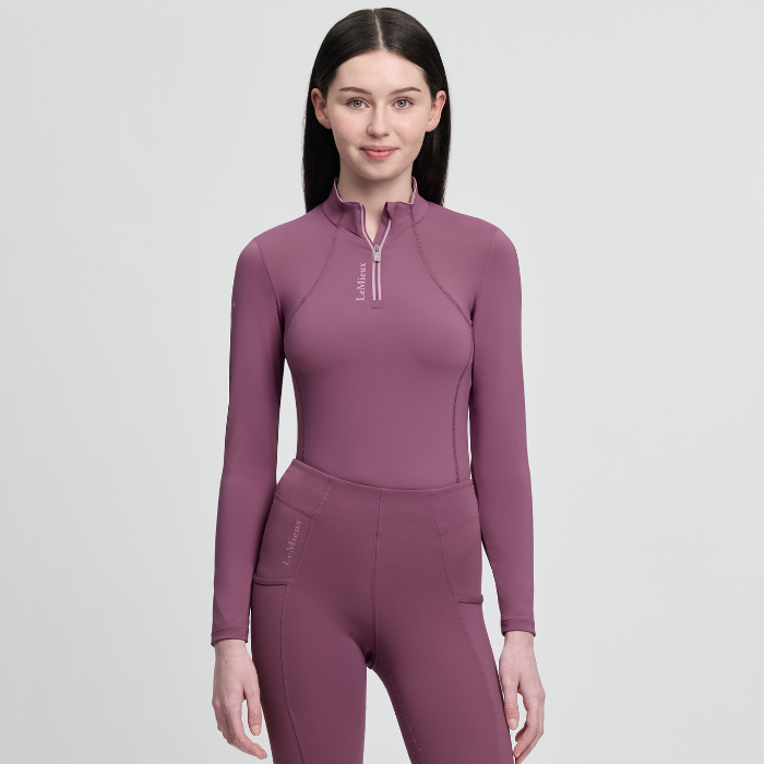 Woman wearing a purple equestrian outfit on a light grey background