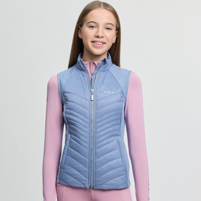 Girl wearing a blue quilted vest over a pink shirt on a light grey background