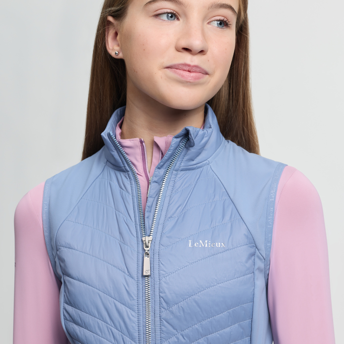 Girl wearing a light blue puffer vest with a visible brand logo on a plain background