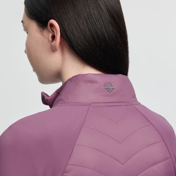 Person wearing a pink quilted jacket with a brand logo on a light grey background