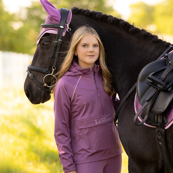 Woman in a pink outfit standing next to a horse in a field
