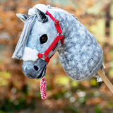 Grey hobby horse wears a red headcollar with matching rope in a blurred outdoor setting