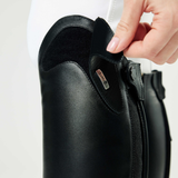 Close-up of a person adjusting a black equestrian boot with a visible brand label on a white background.