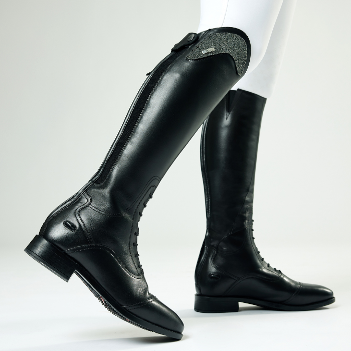 Black riding boots worn with white leggings on a light grey background