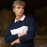 Man wearing a navy sweater with a logo, standing against a dark background