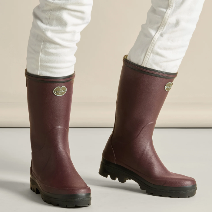 Cherry red rain boots with brand logo worn by a person on a neutral background