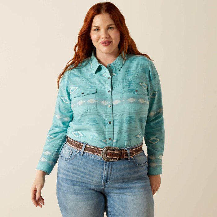 Woman wearing a turquoise patterned shirt and blue jeans on a beige background