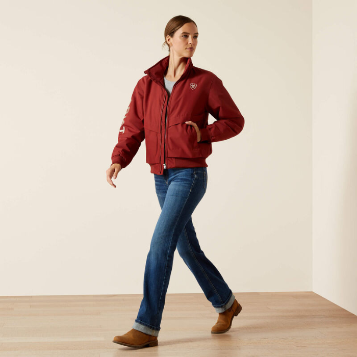 Woman wearing a brown jacket with a logo, blue jeans, and brown shoes on a light background
