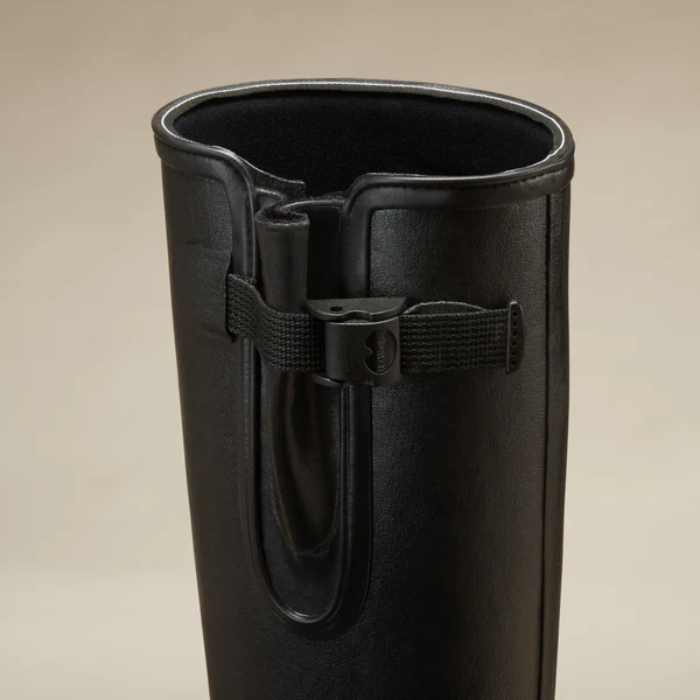 Black leather boot with a strap on a beige background