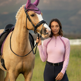 Woman in a pink equestrian shirt standing next to a horse in a field
