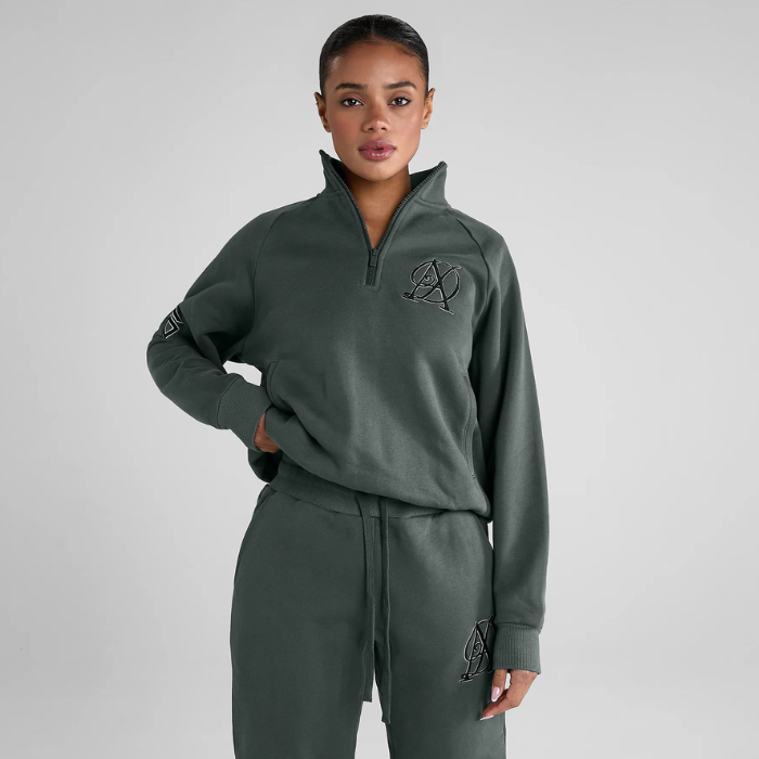 Woman wears a green tracksuit with brand logo on a grey background