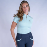 Woman wearing a light blue equestrian shirt and navy leggings on a white background