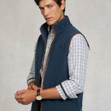 Man wearing a blue gilet over a plaid shirt with a neutral background