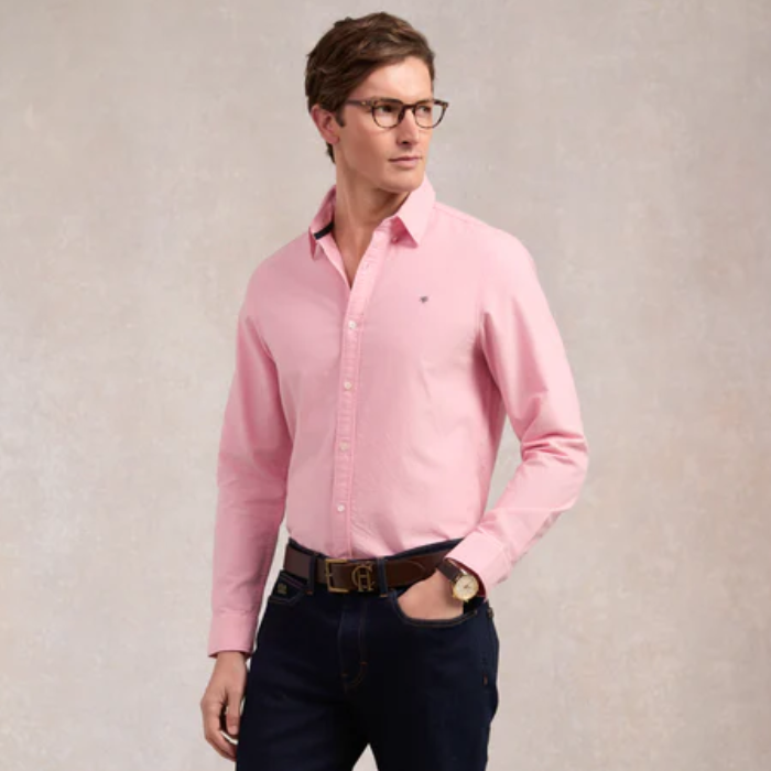 Man wearing a soft pink shirt with dark trousers on a plain background