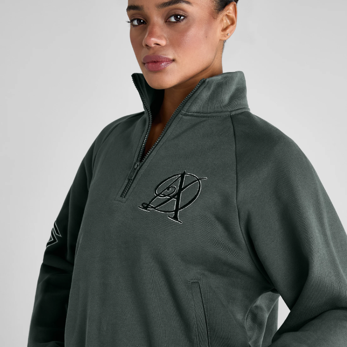Woman wears a green sweatshirt with AD logo on a grey background