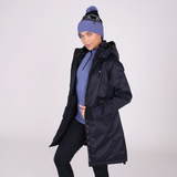 Woman wears a black coat unzipped with a blue sweater and hat on a light background
