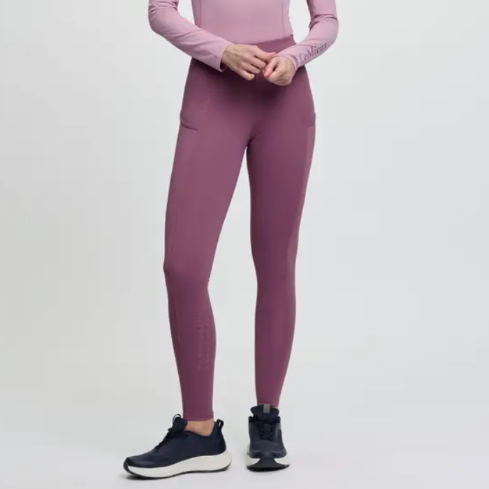 Pink riding leggings with black trainers on a grey background