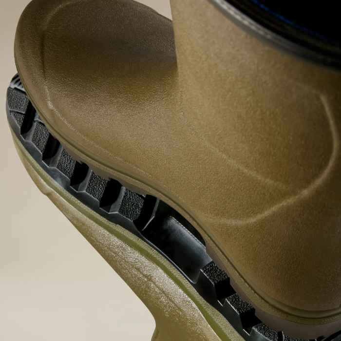 Close-up of a green rubber boot with a black sole on a beige background