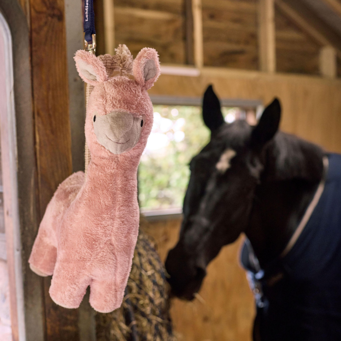 Pink plush llama toy hanging in a stable with a horse in the background