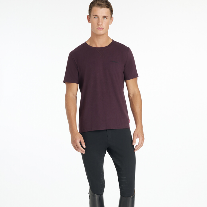 Man wears a purple t-shirt and black breeches on a white background